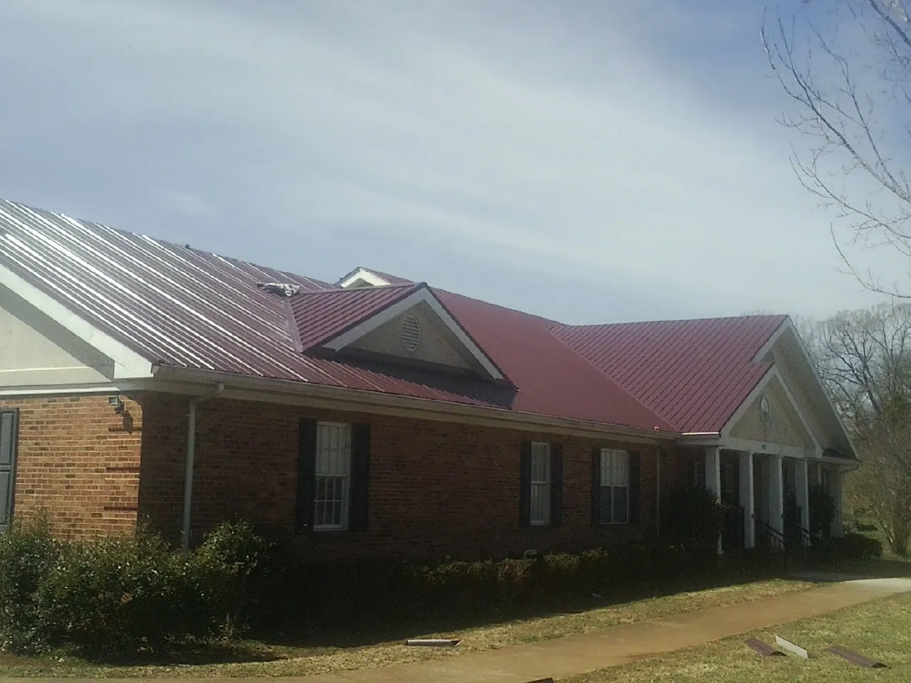 Red metal roof with gabled entries on a long brick building, from a Hail Damage Roof Repair job in Richeyville