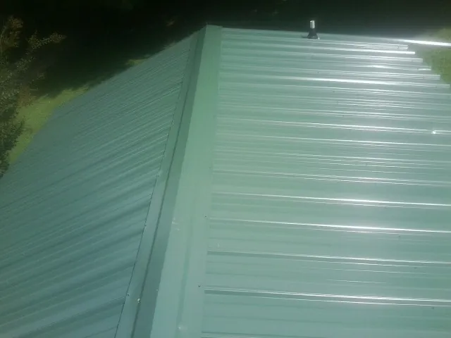 New green metal panels meeting at the ridge of a roof — Flat Roof Repair work by our crew in Richeyville