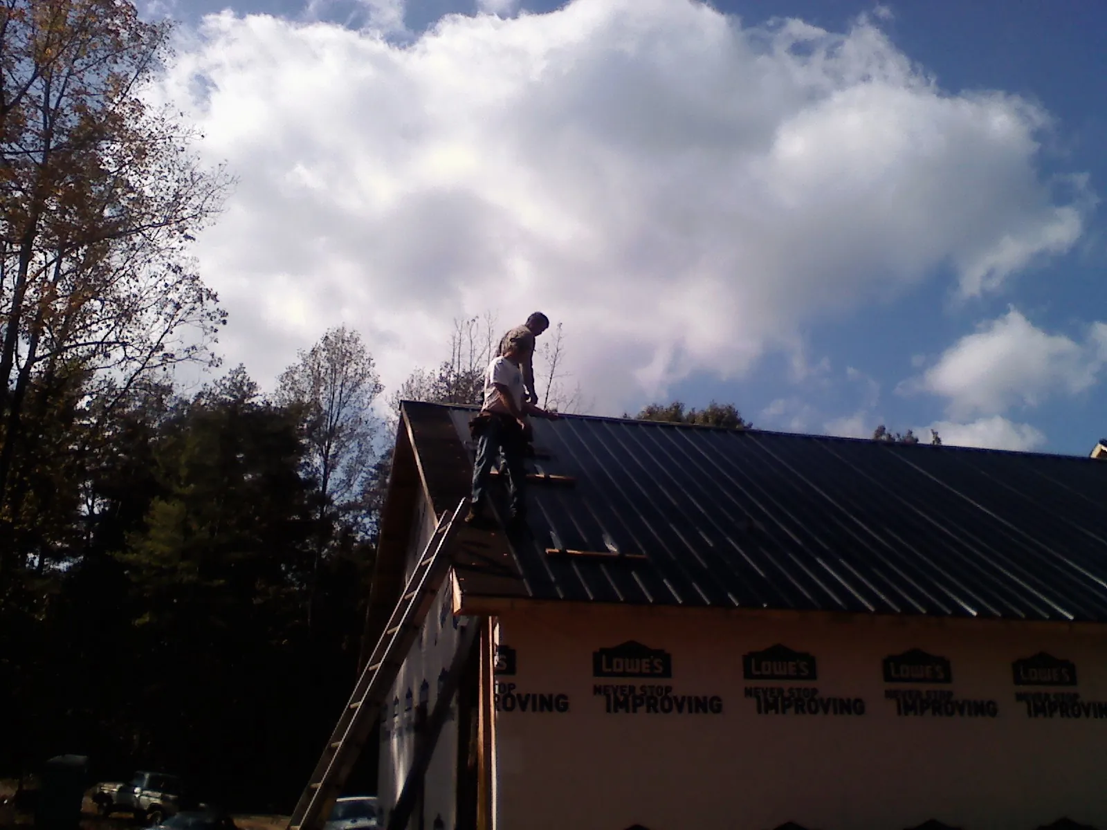 Roofer fastening dark metal panels high against a cloudy sky, from a Roof Inspection job in Richeyville