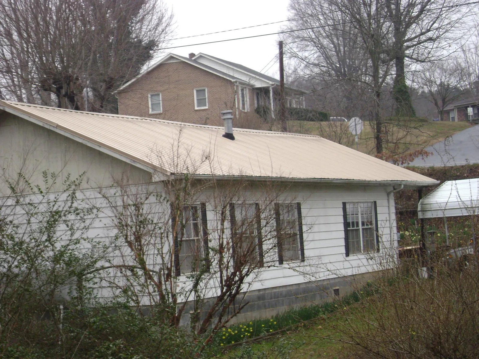 Tan metal roof on a white sided house set into a hillside — Commercial Roofing by Roofing Brothers in Richeyville